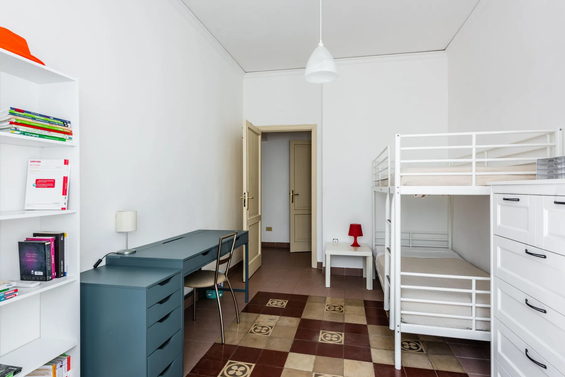 A bedroom with bunk beds, a desk, and white shelving.