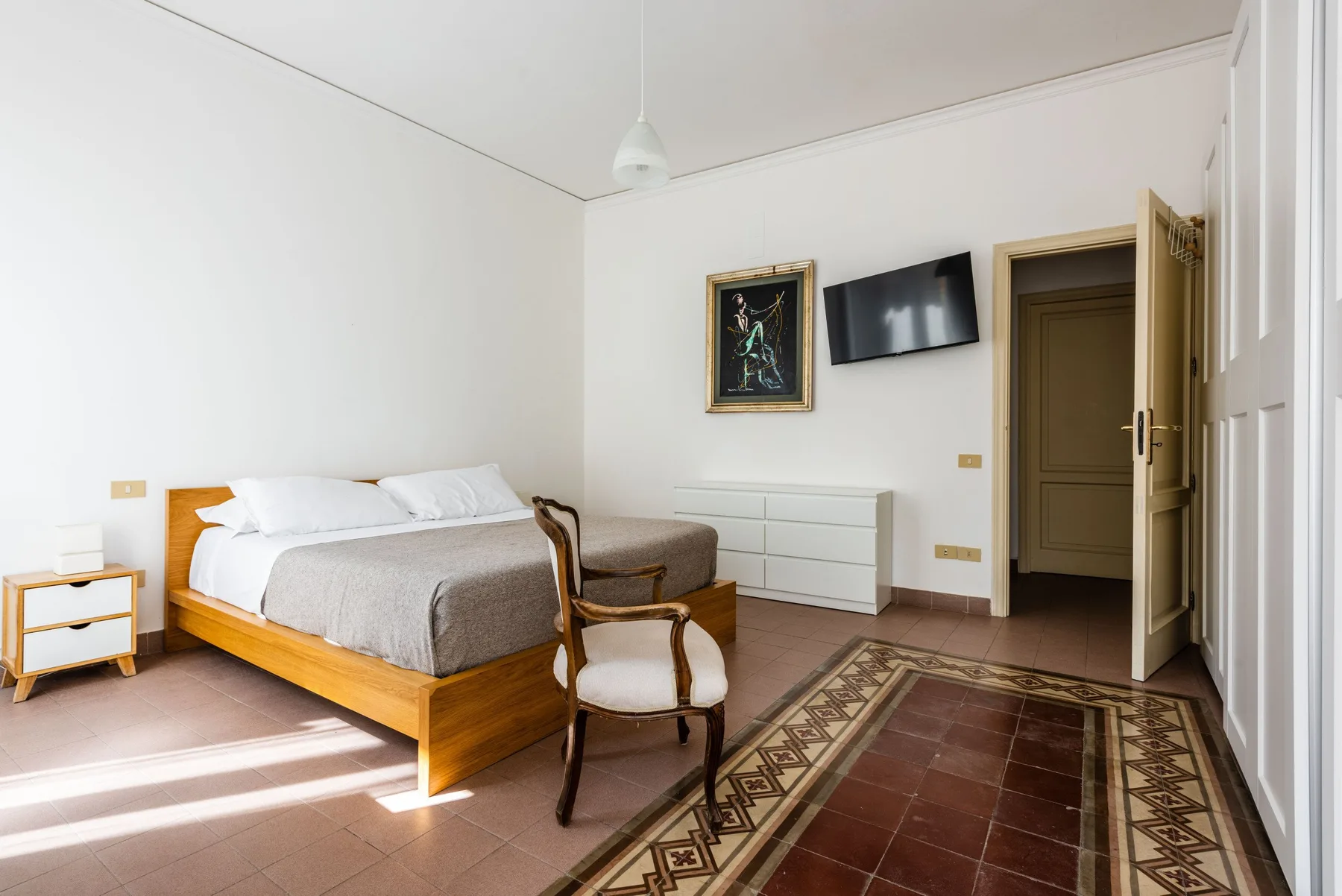 A bedroom with a wooden bed, a chair, and a patterned rug.