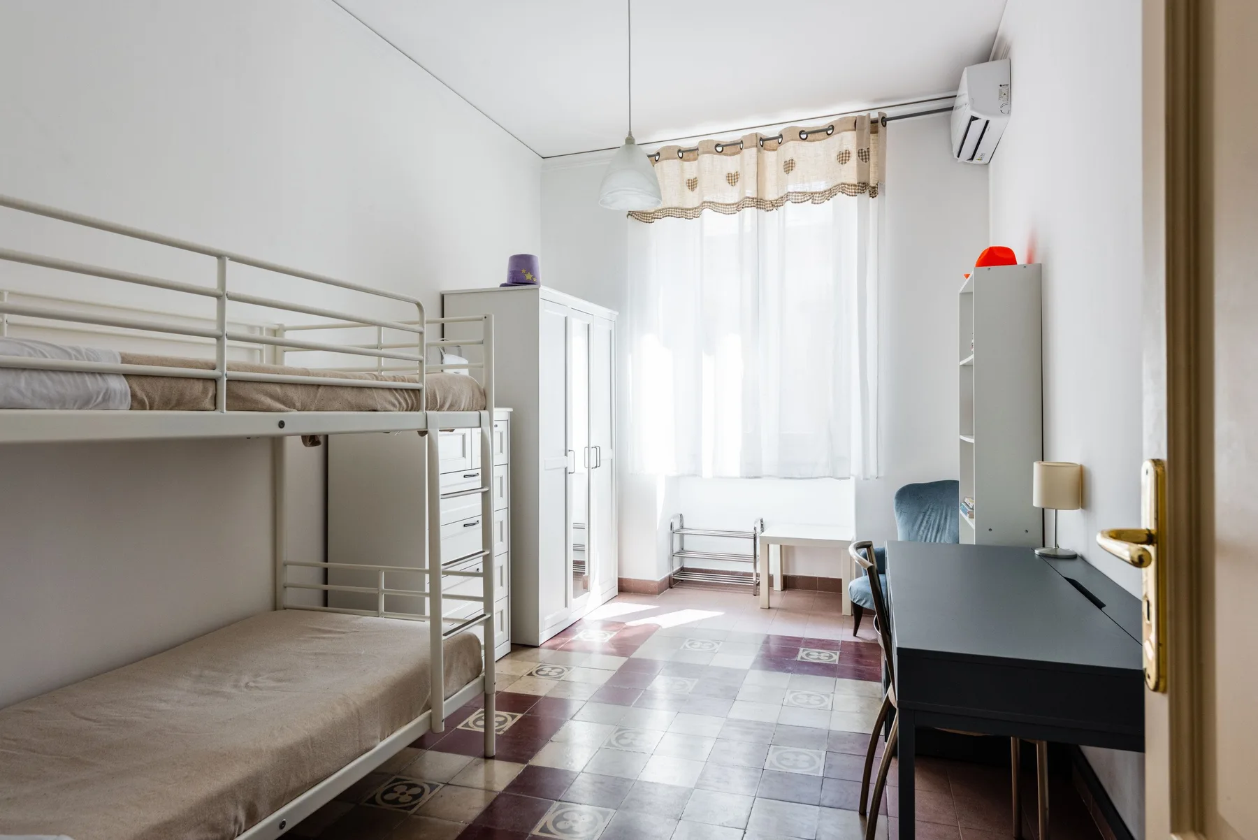 A bright bedroom with bunk beds, a desk, and a large window.