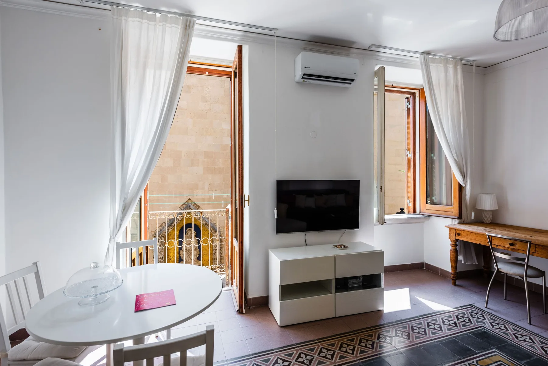 A bright living room with a television and an open balcony door.