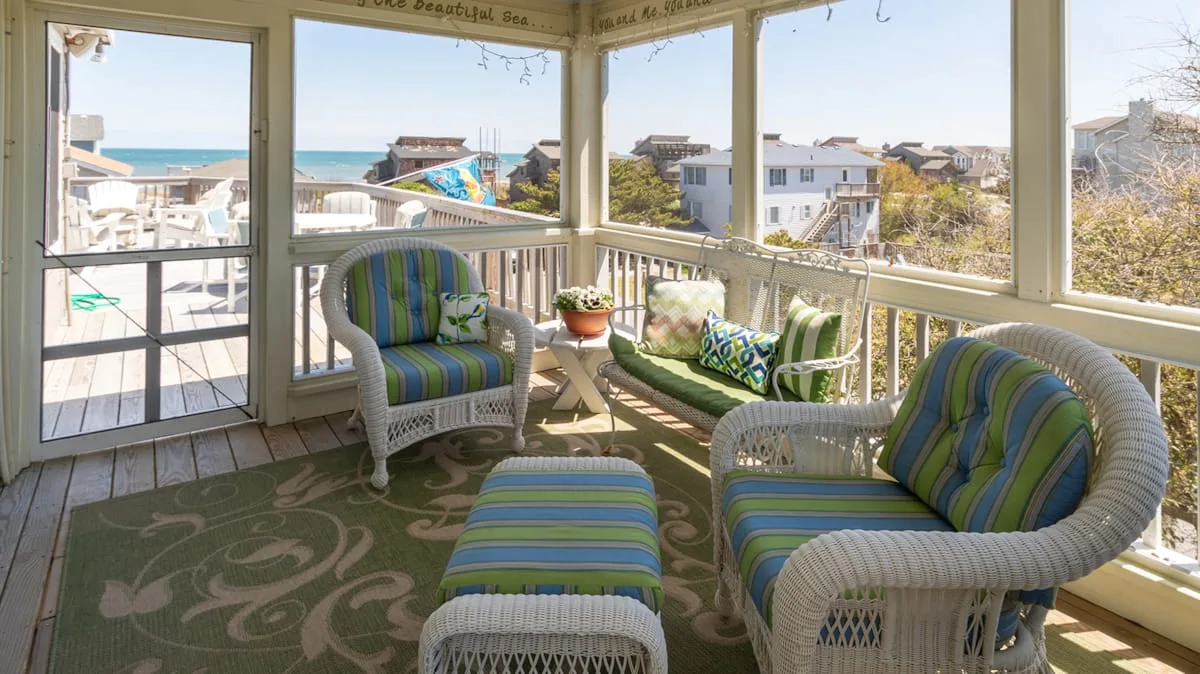 A sunroom seating area with striped cushions and views of the ocean and nearby homes.