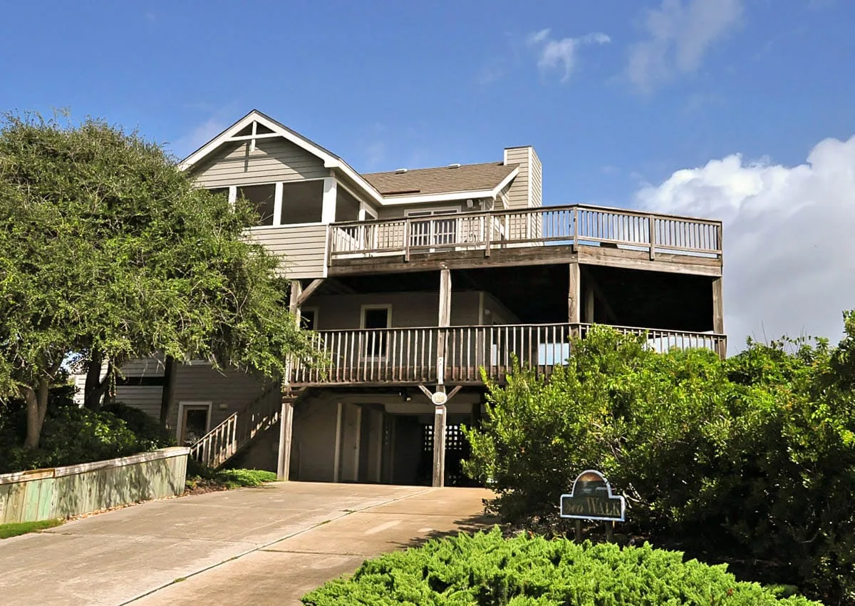 Exterior view of a two-story house with wooden decks and a driveway.