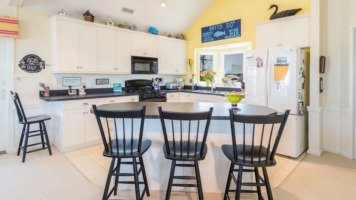 A bright kitchen with white cabinets, a central island, and bar seating.