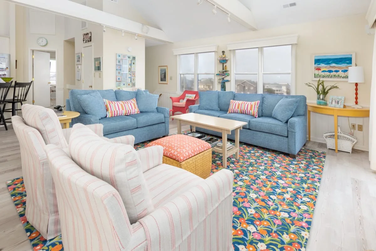 A bright living room with seating arranged around a coffee table on a colorful rug.