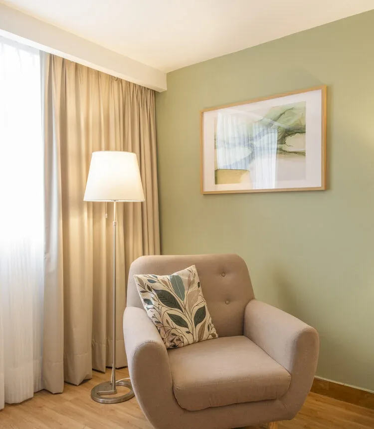 Armchair and lamp beside the window in a Stanza Hotel King room