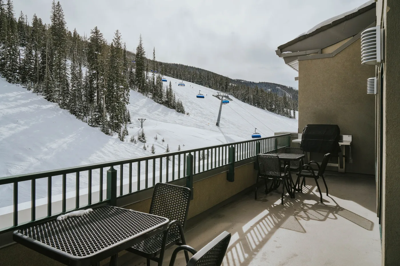 A balcony overlooks a snowy ski slope, with outdoor seating beside the railing.