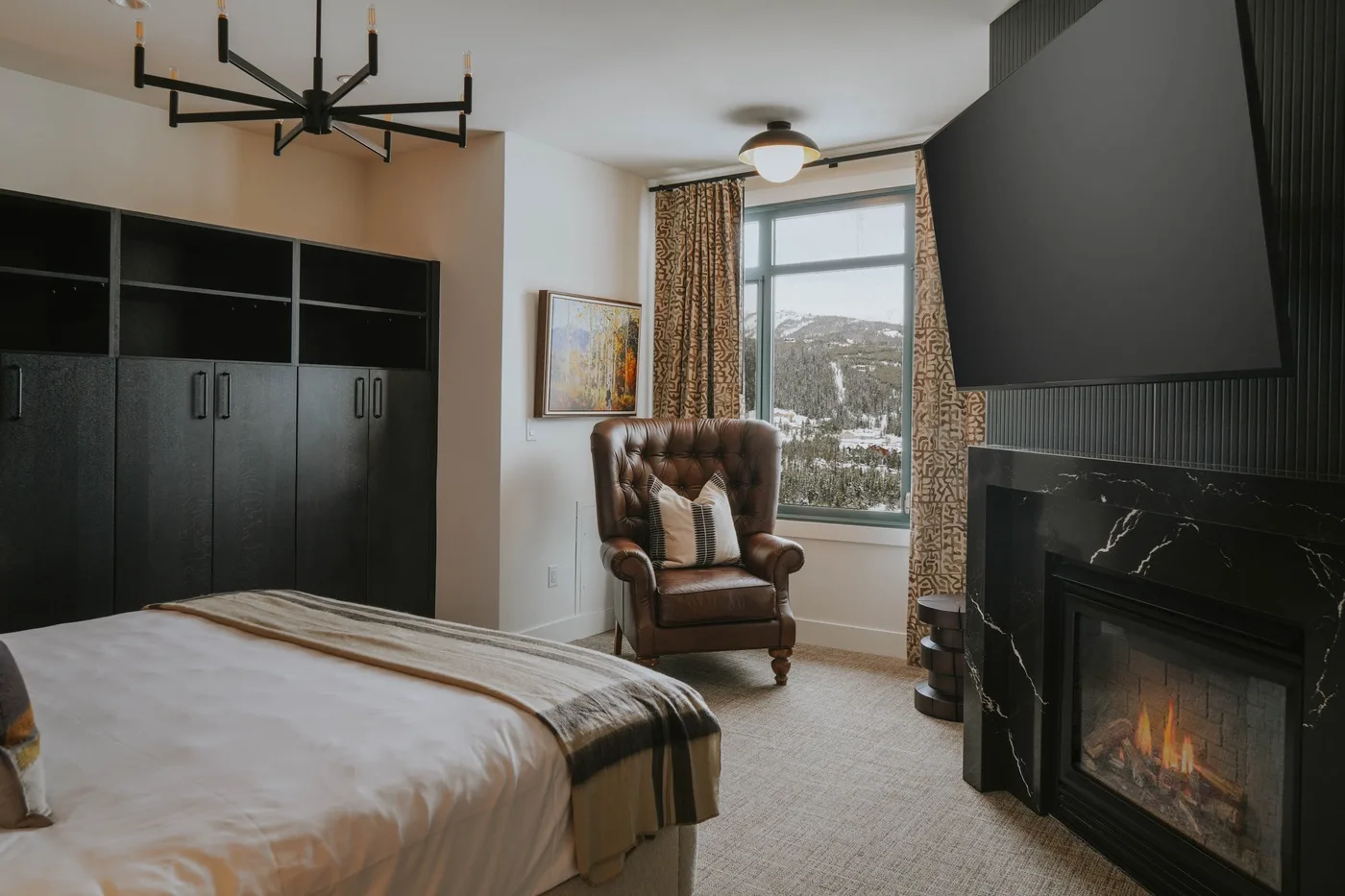 A bedroom with a bed, an armchair, and a fireplace beside a window.