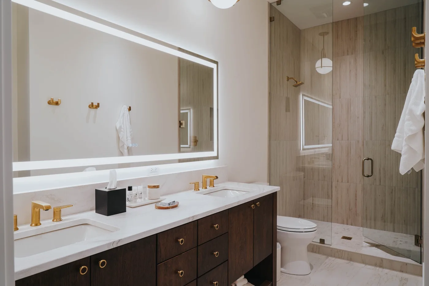 A bathroom vanity with a wide mirror faces a glass-enclosed shower.