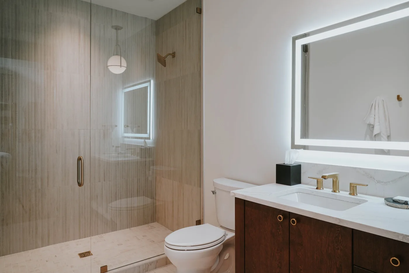 A bathroom with a glass shower and a vanity beneath a large mirror.