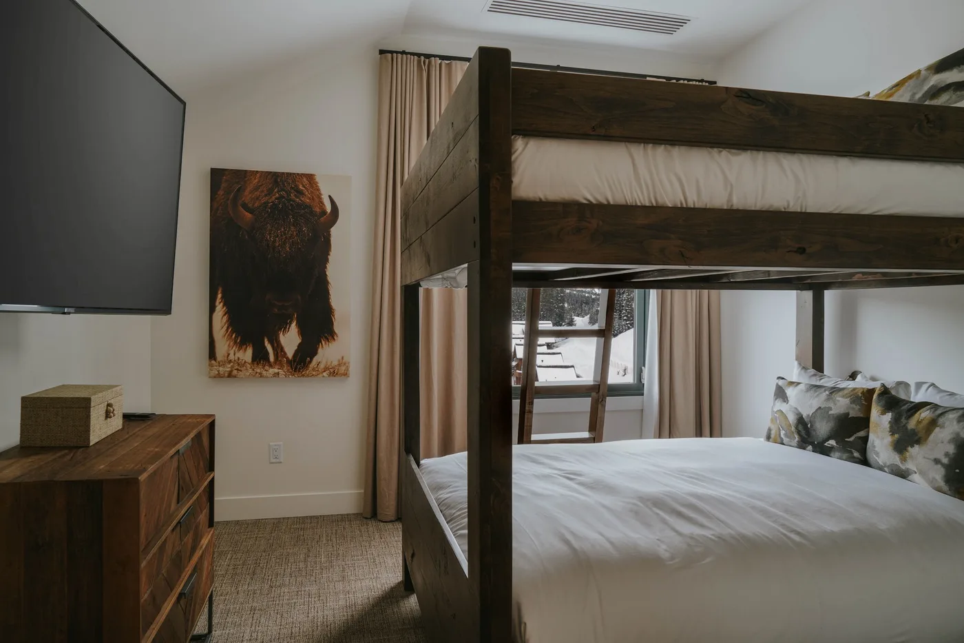 A bedroom with a dark wooden bunk bed, white bedding, and a wall-mounted television.