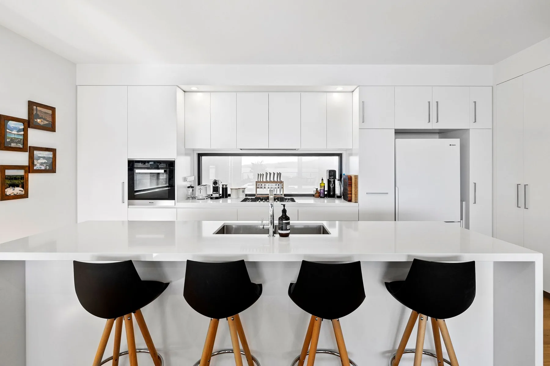Una cocina blanca y luminosa con una isla grande y asientos oscuros.