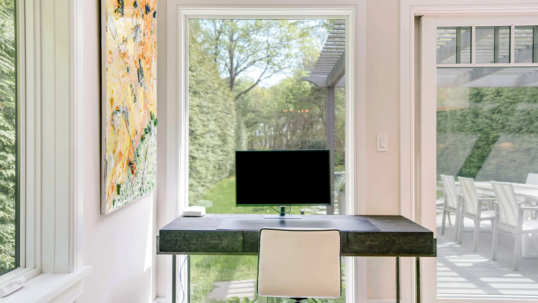 A desk and chair sit between large windows overlooking trees and an outdoor dining area.