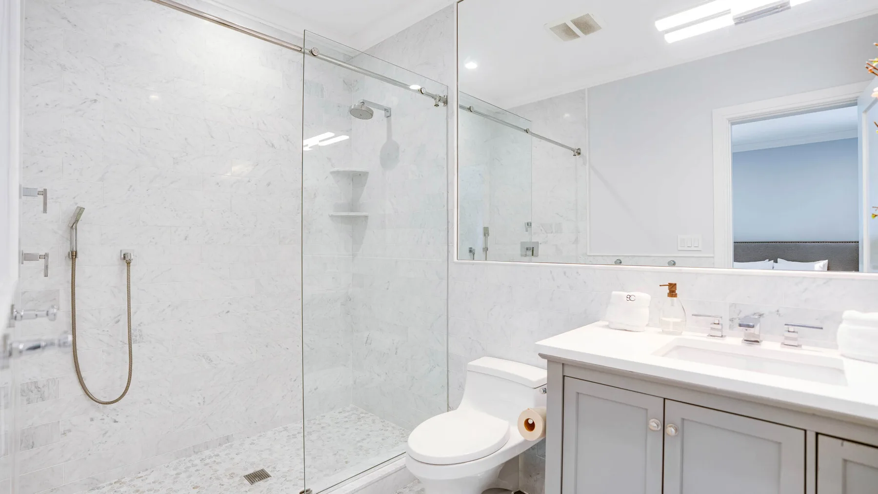 A bright bathroom with a glass shower, toilet, and sink vanity.
