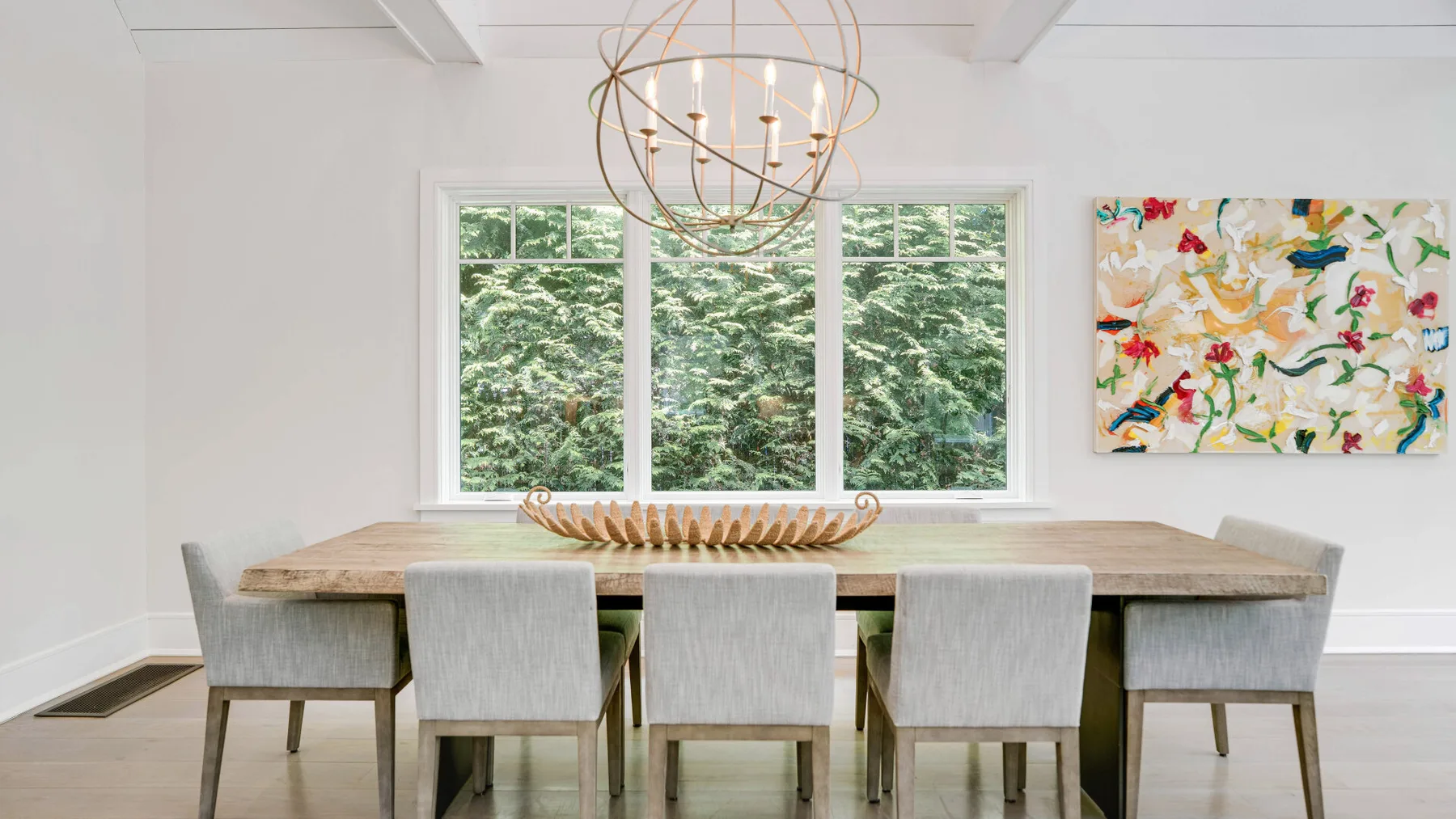 A dining area with a long table, seating, and a large window overlooking greenery.