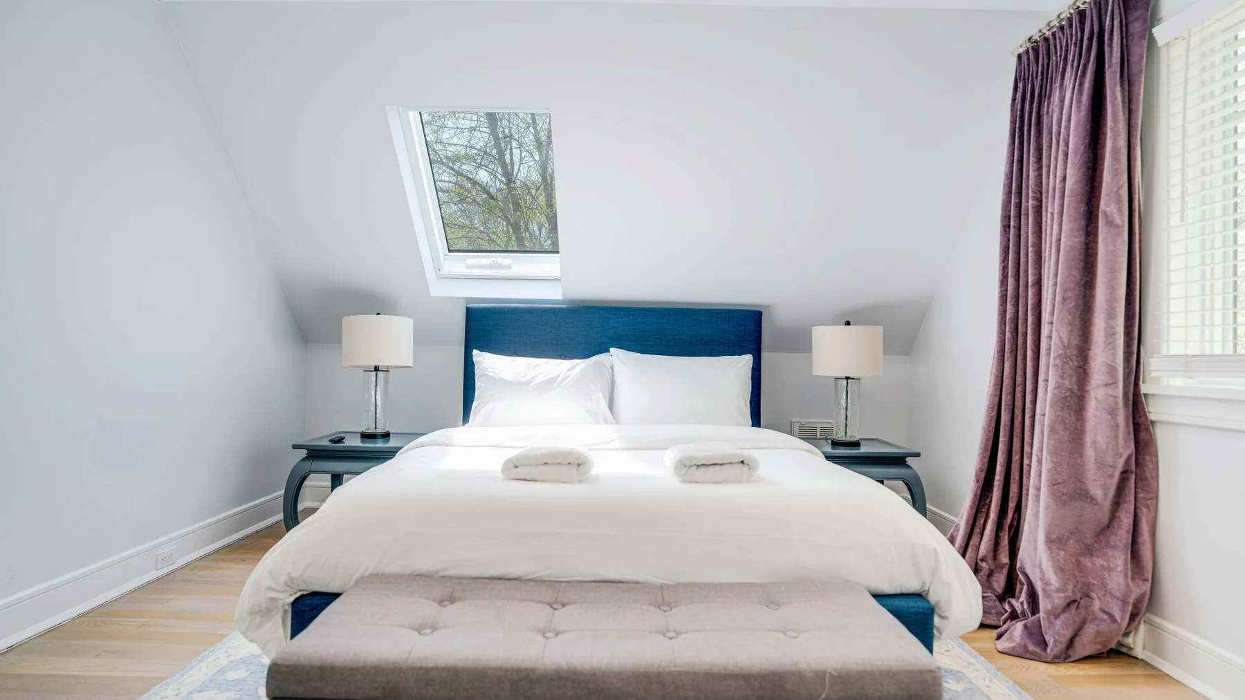 A bright bedroom features a neatly made bed and a cushioned bench.