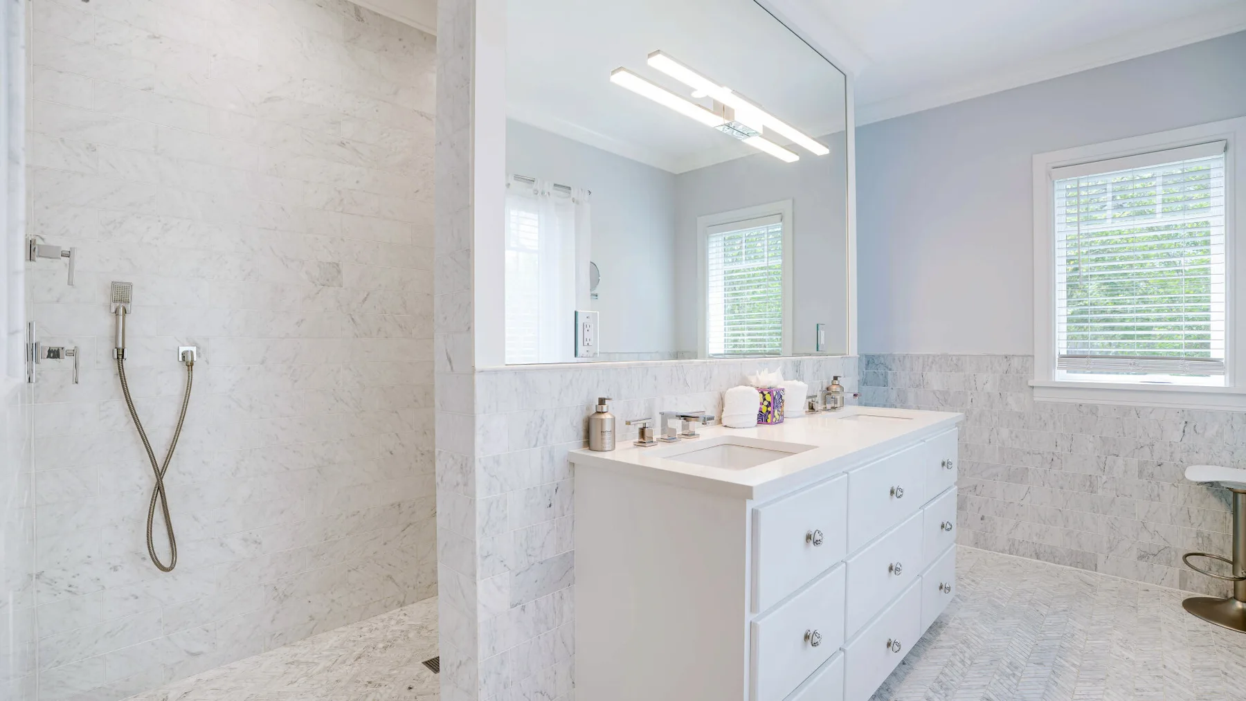 A bright bathroom with a white vanity, large mirror, and shower area.