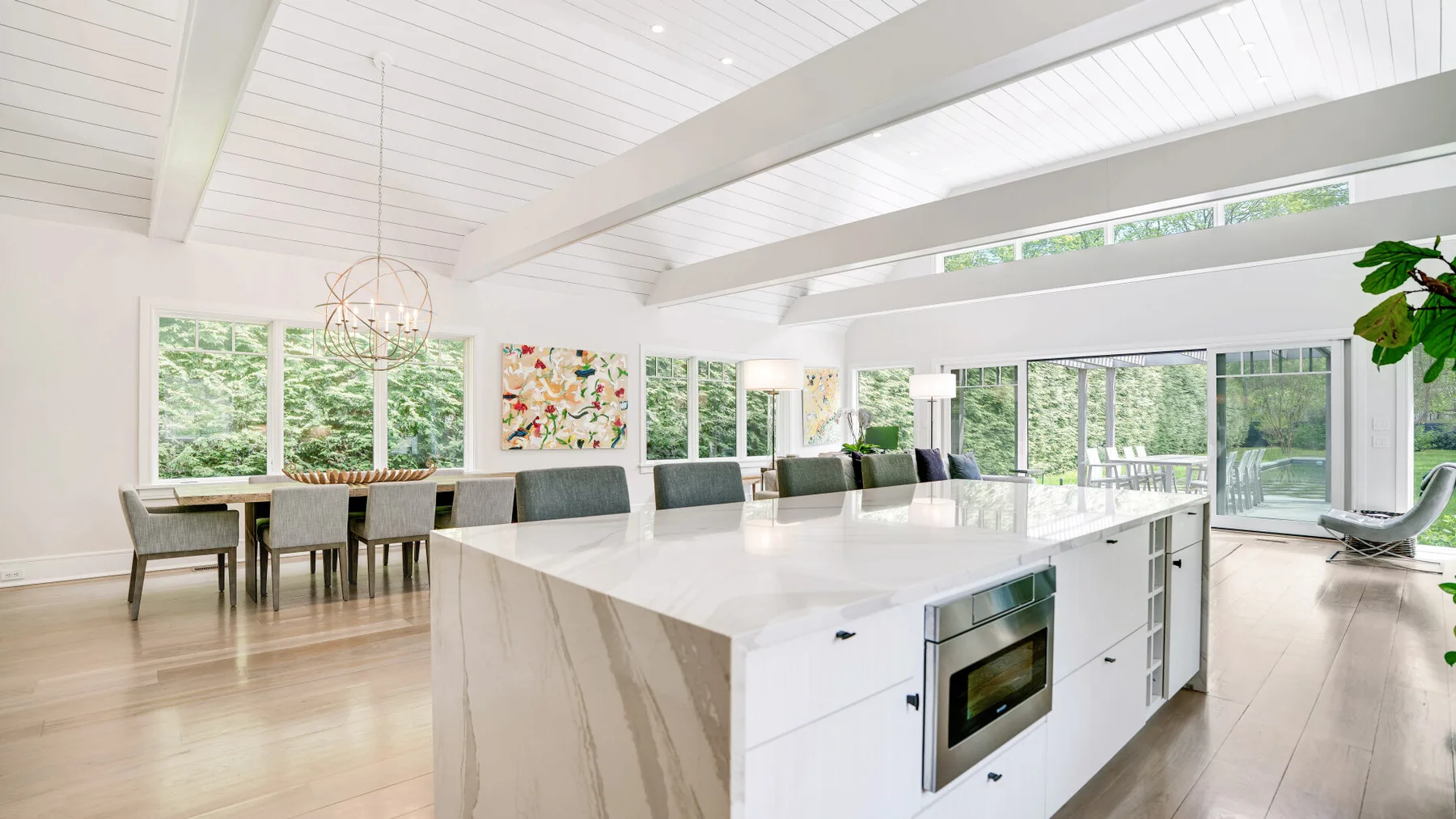 A bright open kitchen features a large island and windows overlooking greenery.