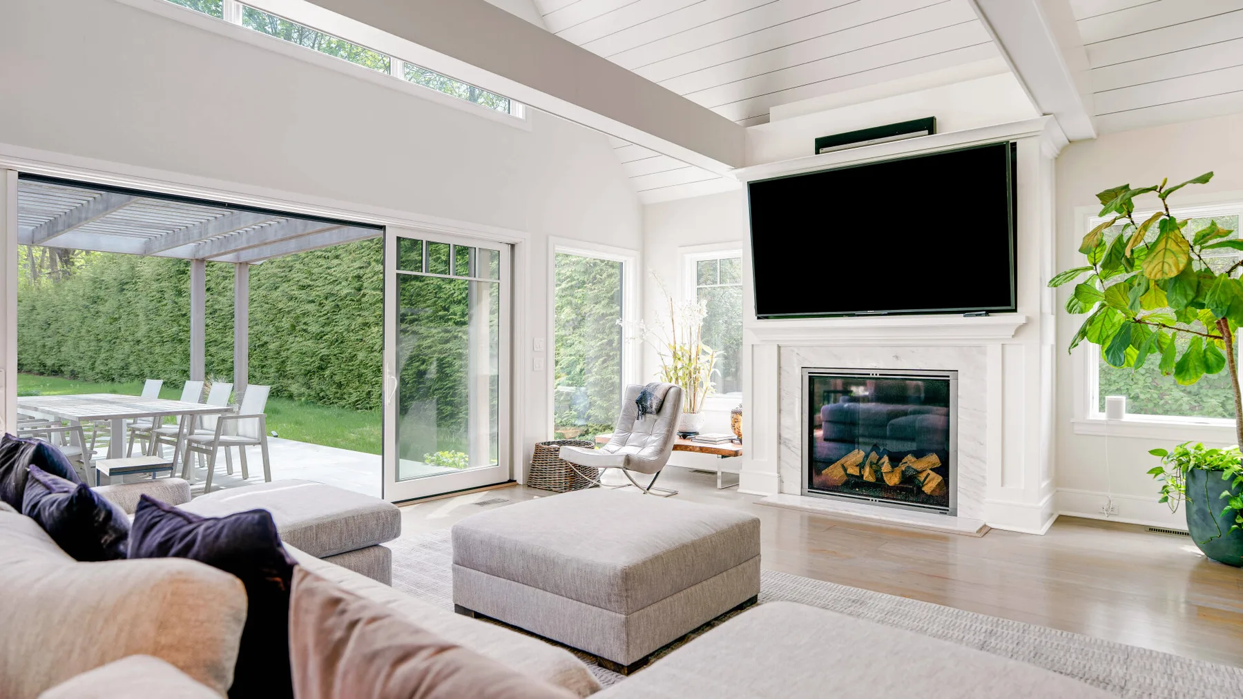 A bright living room with large windows, a fireplace, and an ottoman.
