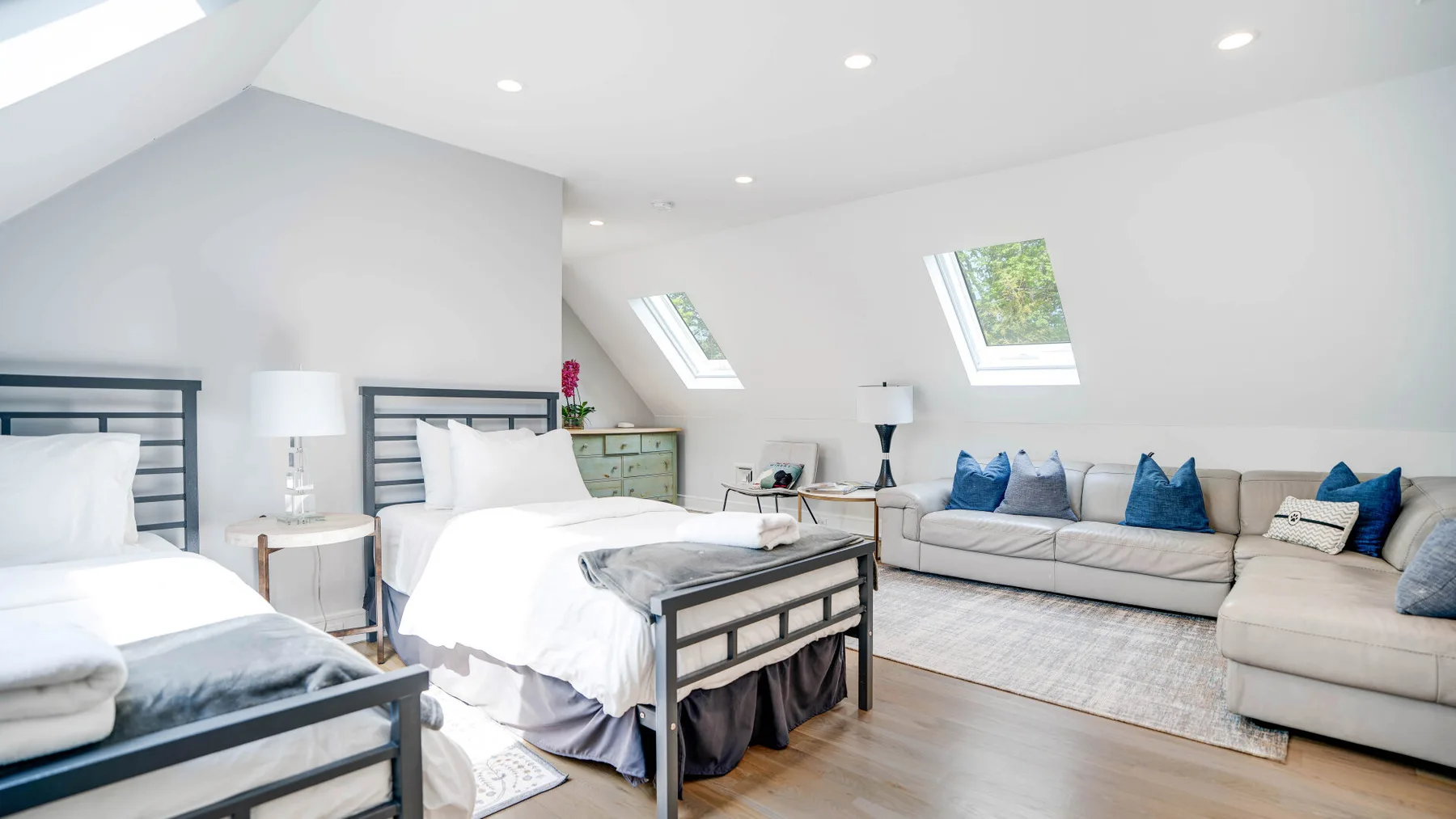 A bright bedroom with two beds and a seating area beneath skylights.