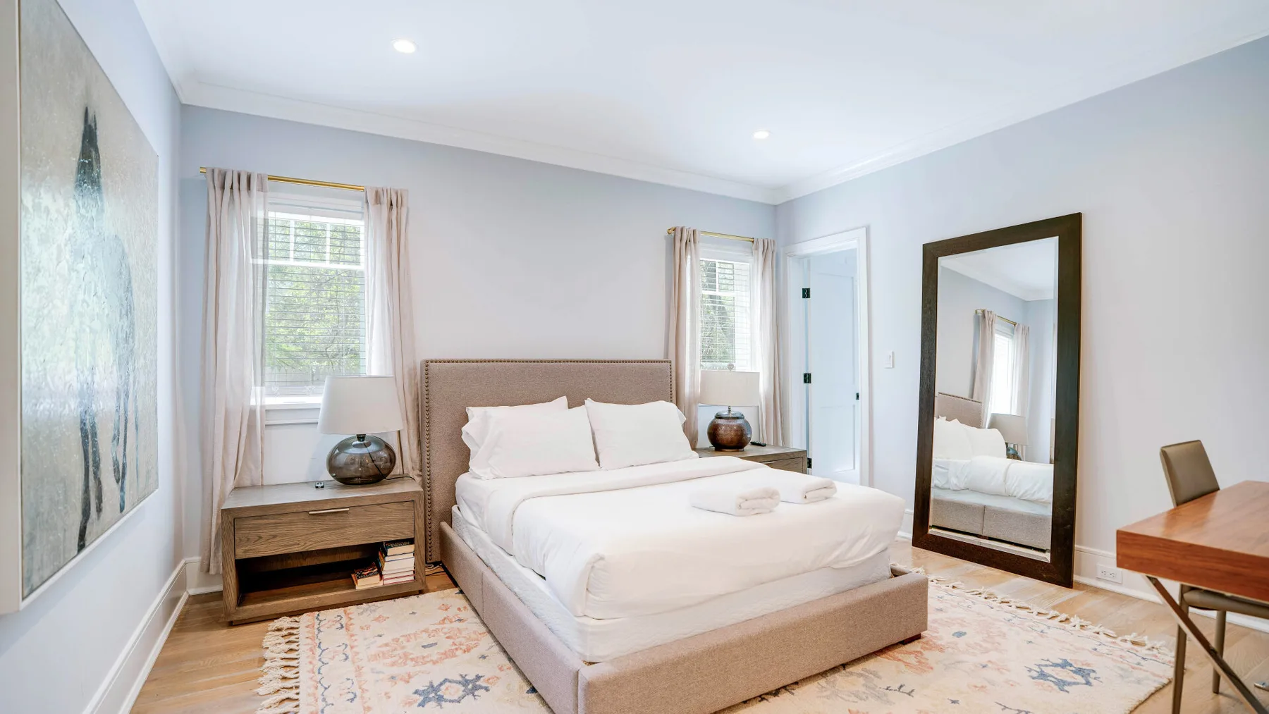 A bright bedroom with a neatly made bed and large framed artwork.