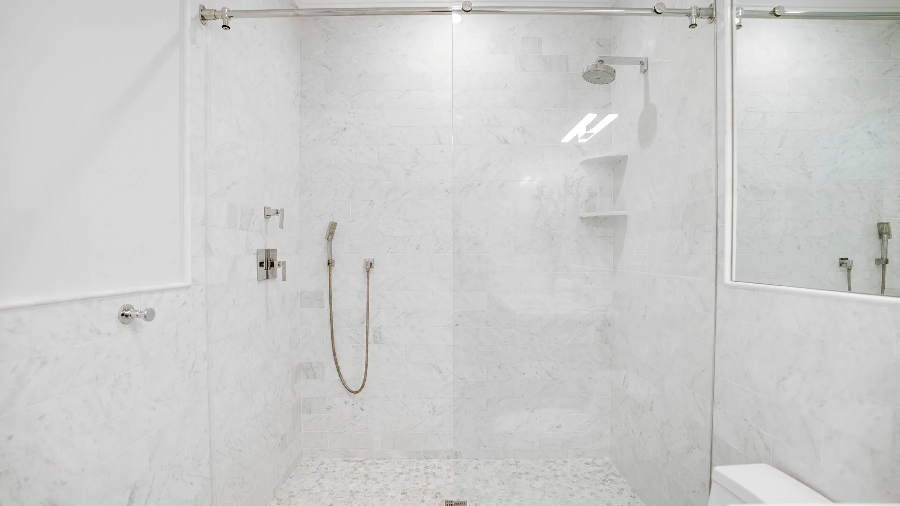 A bright bathroom with a walk-in shower and pale tiled walls.