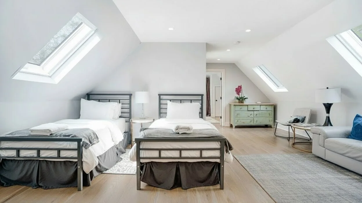 A bright attic bedroom with two beds beneath sloped ceilings and skylights.