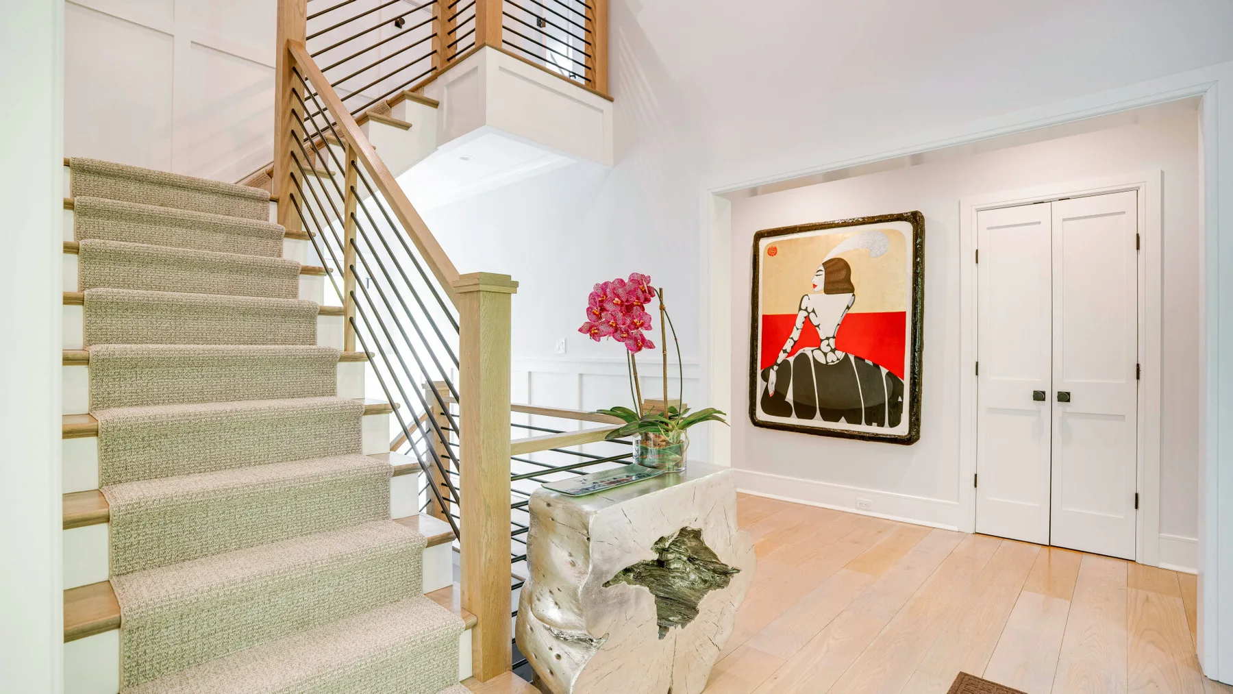 A bright stairwell with carpeted stairs, a metal railing, and wall art.