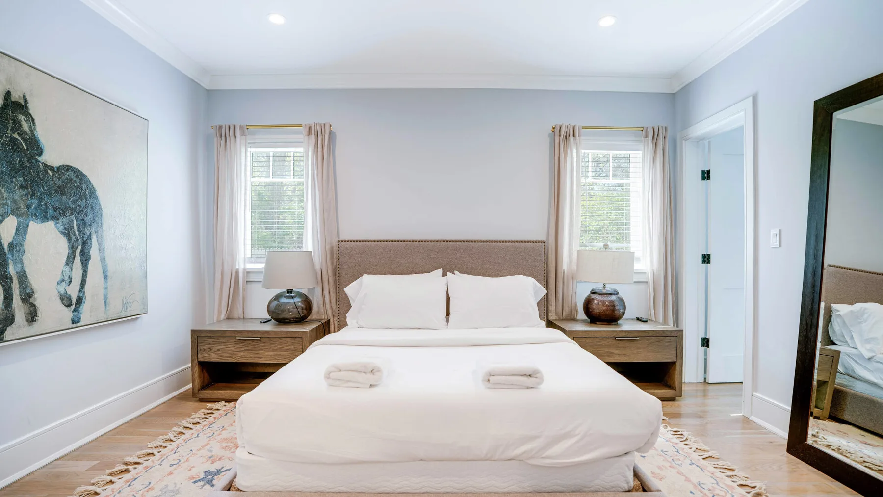 A bright bedroom with a neatly made bed between two windows.