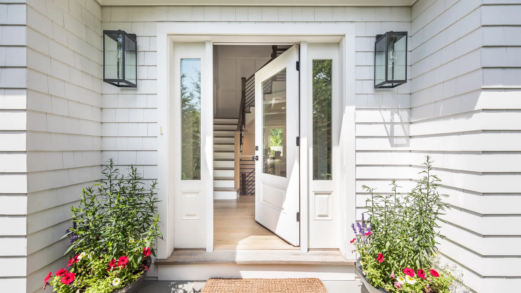 A white house entrance with an open door and flower planters.
