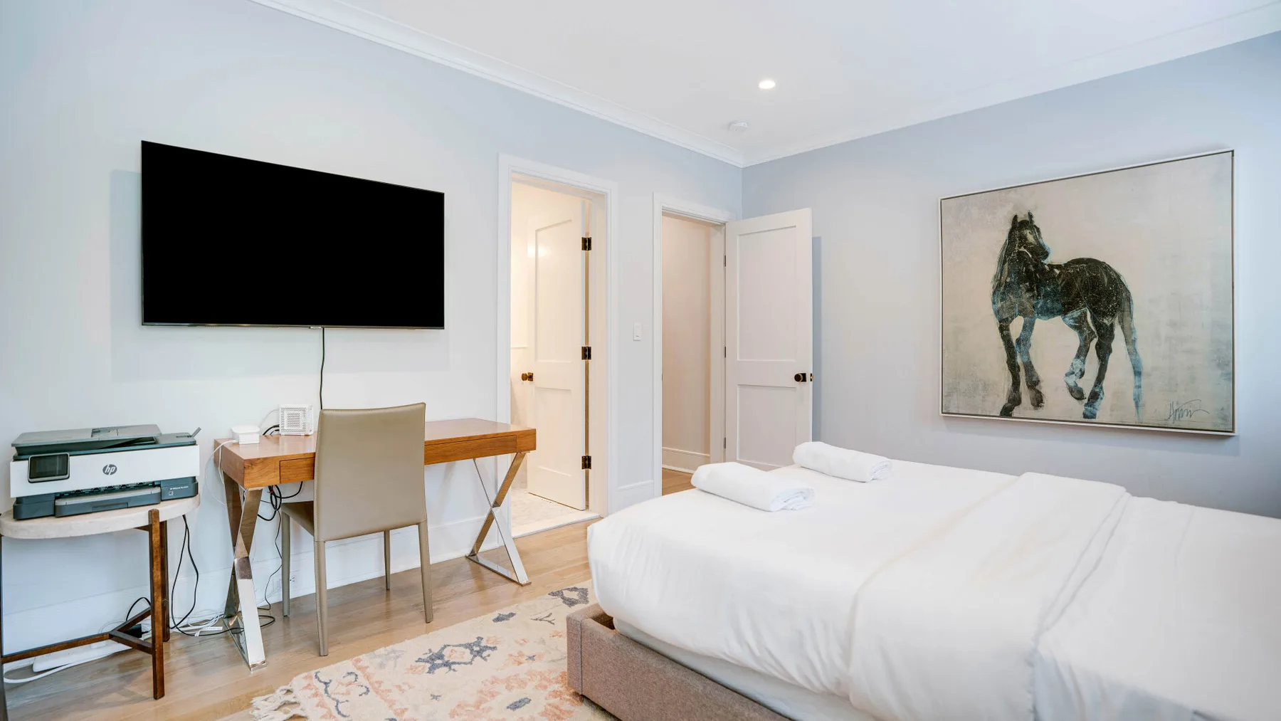 A bedroom with a white bed, wall-mounted television, and desk.