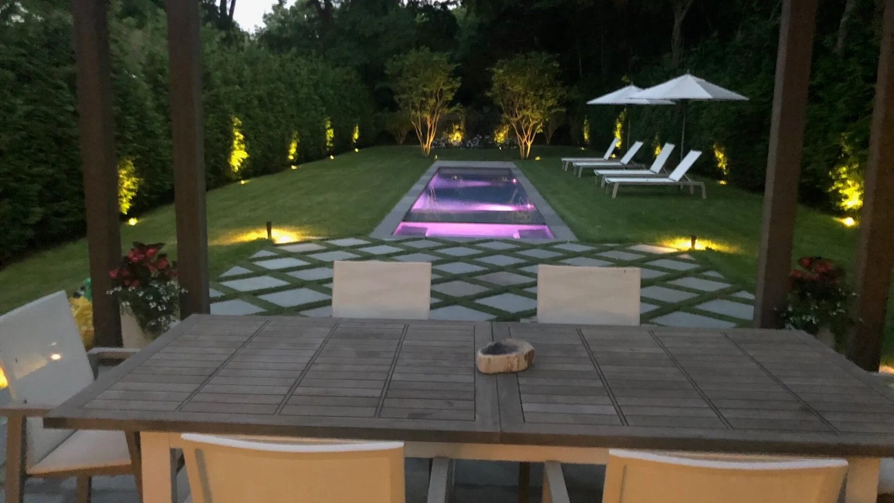 A landscaped garden patio overlooks a lit swimming pool, with outdoor seating nearby.