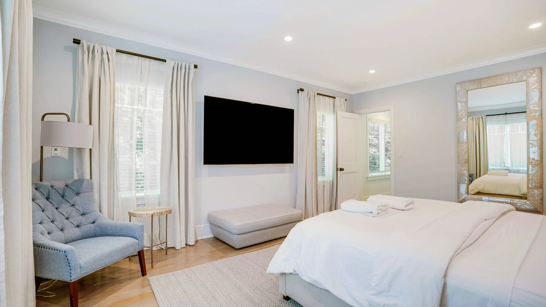 A bright bedroom with a neatly made bed and a wall-mounted television.