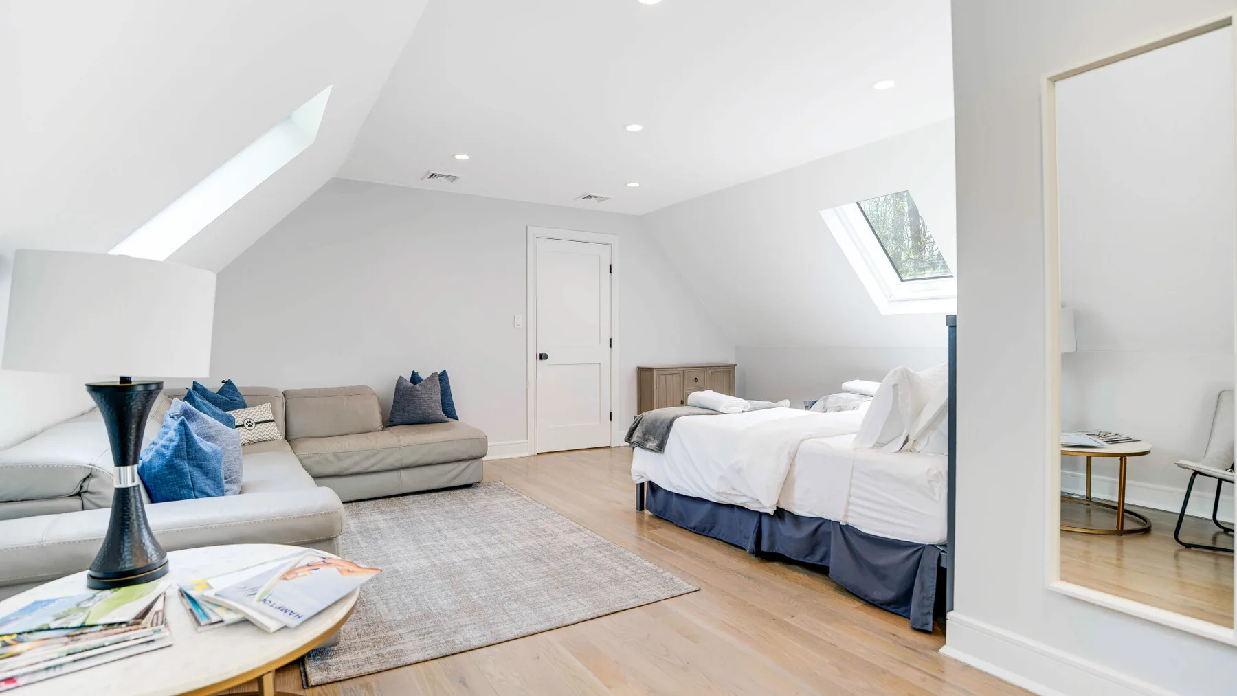 A bright attic bedroom with a bed, seating, and sloped ceilings.