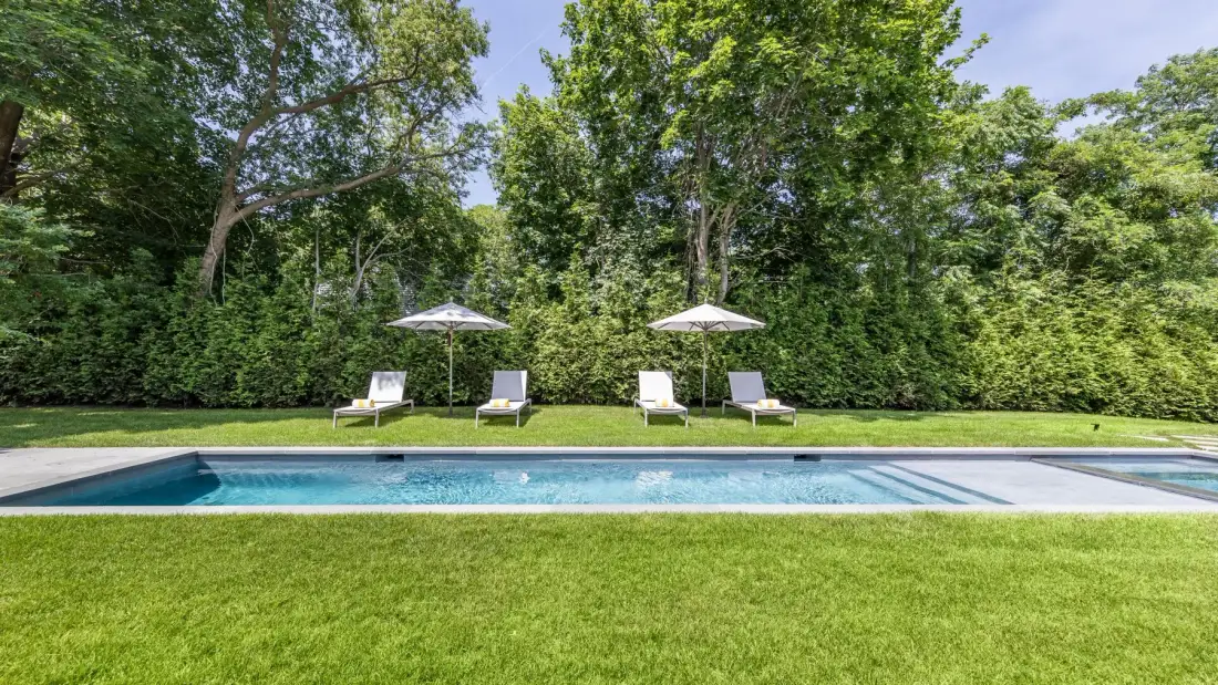 An outdoor swimming pool sits beside a lawn, with lounge chairs and umbrellas.