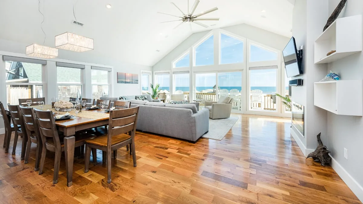 Una luminosa sala de estar y comedor de concepto abierto, con grandes ventanas y suelo de madera.