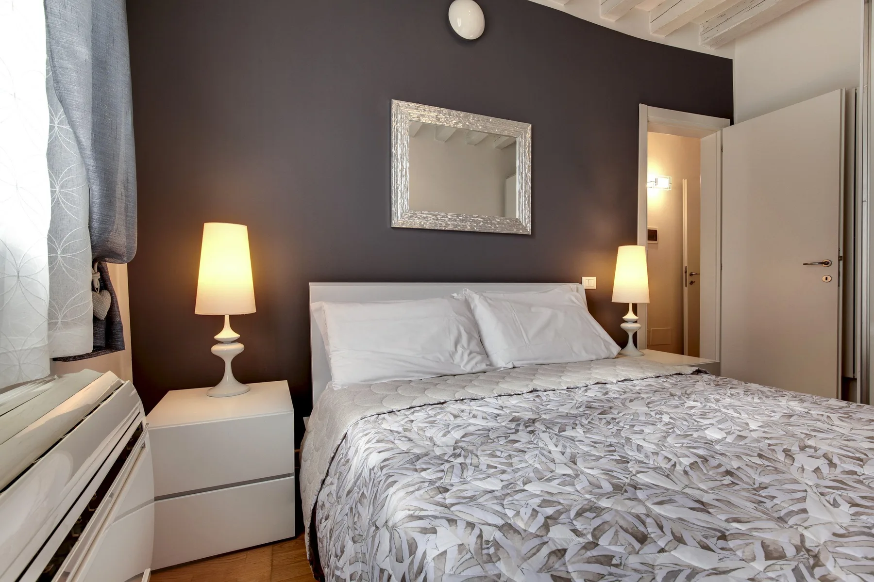A bedroom with a large bed, patterned bedding, and matching bedside lamps.