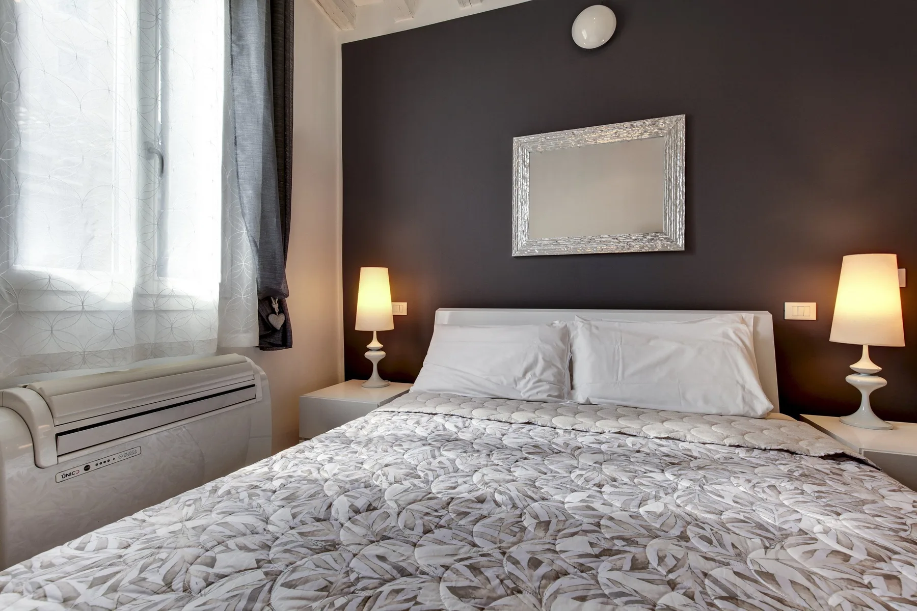 A bedroom with a bed, patterned bedding, and a framed mirror above the headboard.