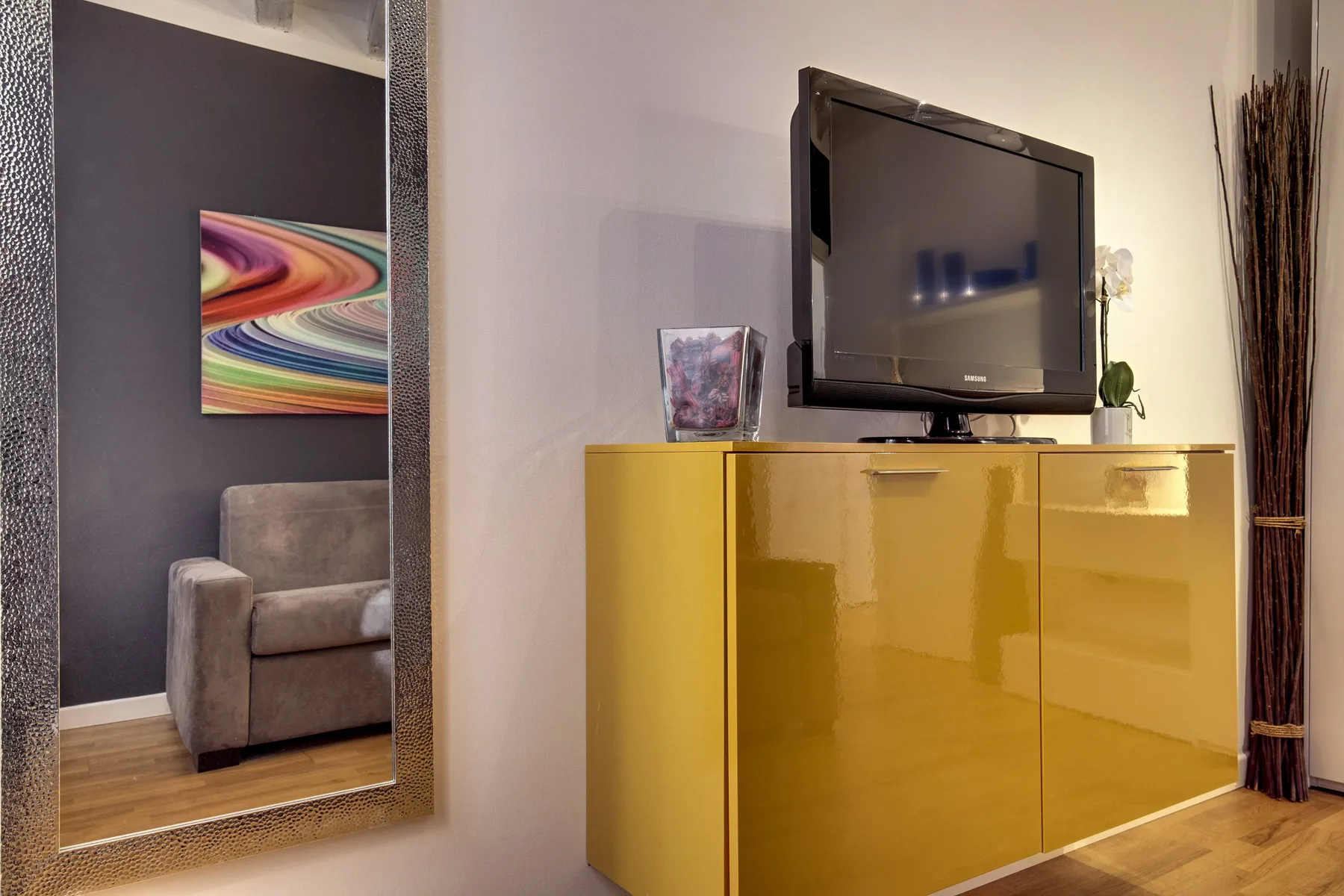 A television sits on a glossy yellow cabinet beside a large wall mirror.