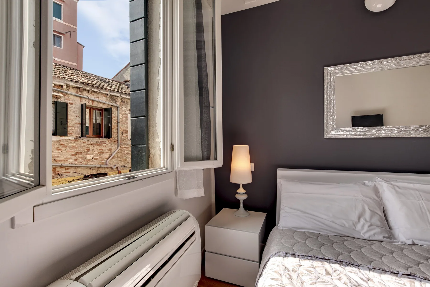 A bedroom with a bed beside an open window and a bedside lamp.