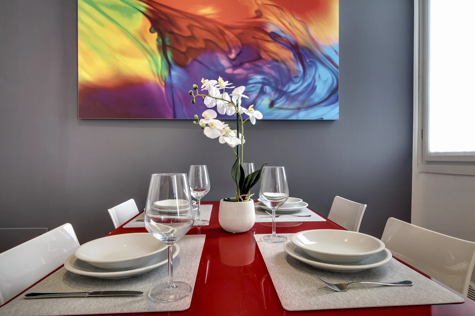 A dining table is set with plates and glasses beneath colorful abstract artwork.