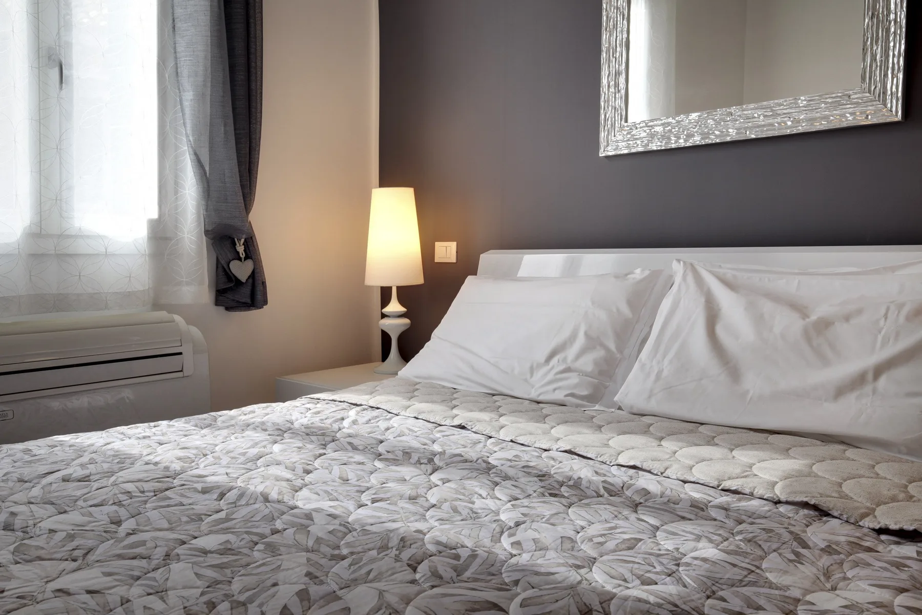 A bedroom with a made bed, a bedside lamp, and a window.