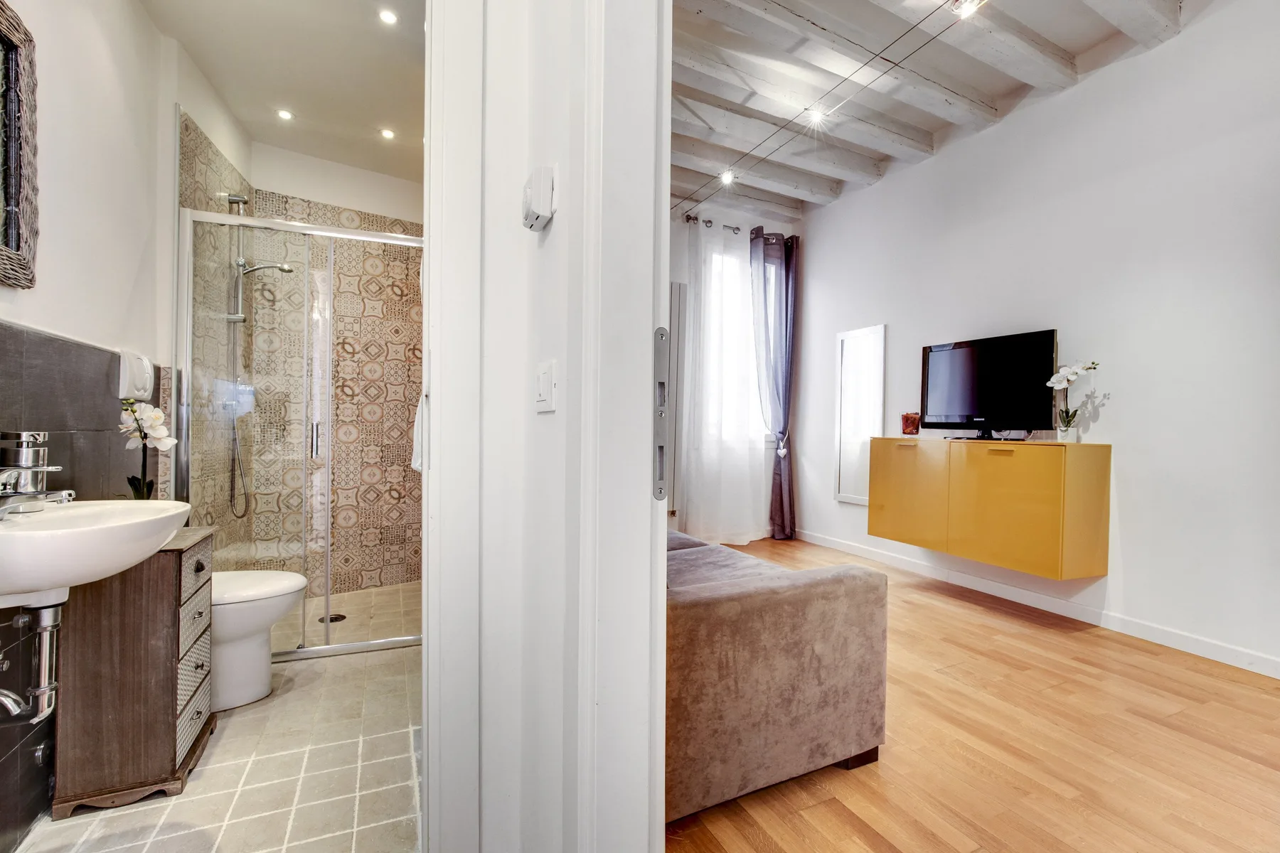 A bathroom opens onto a living area with a wall-mounted television and cabinet.