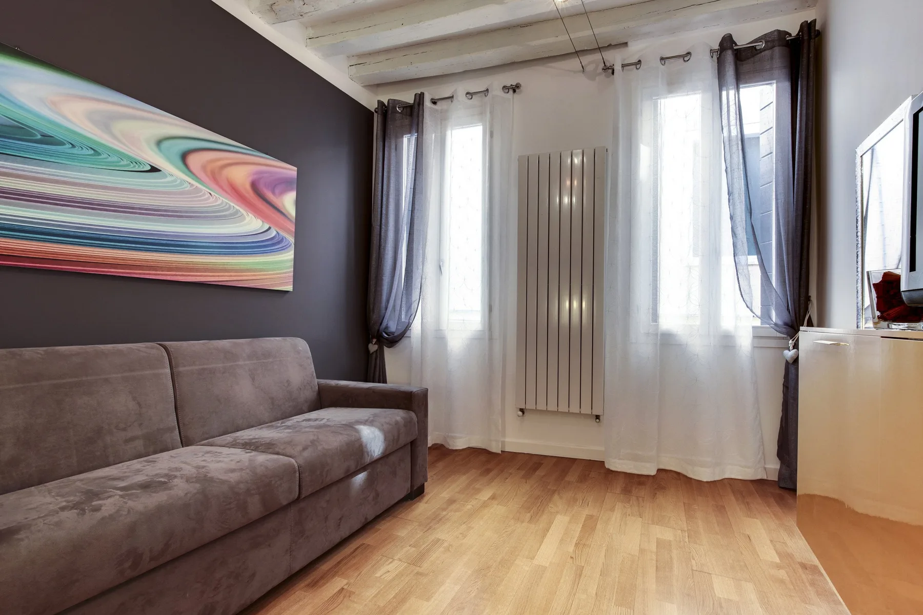 A living room with a gray sofa, colorful wall art, and tall windows.
