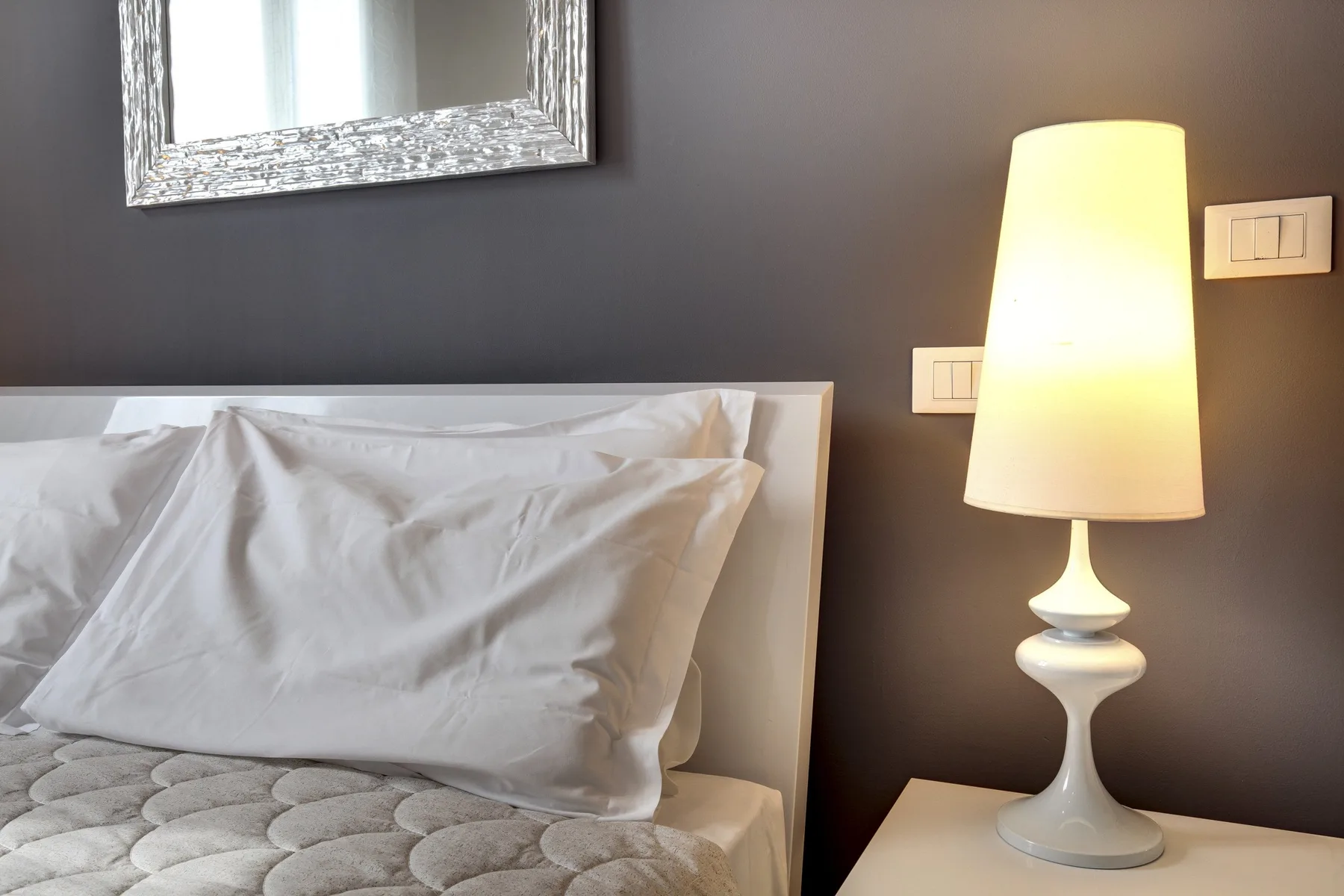 A bedroom scene with a bed, pillows, and a lit bedside lamp.