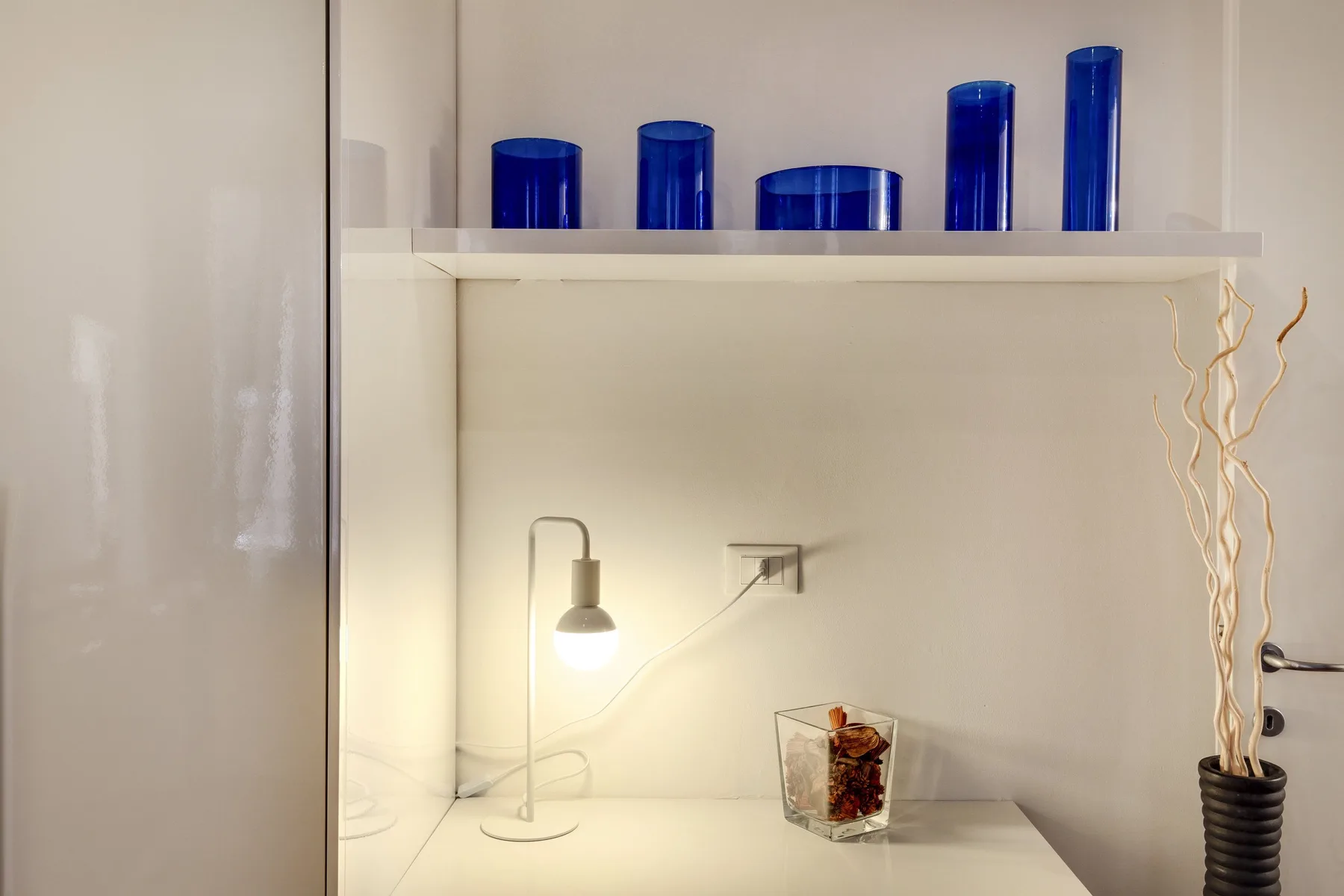 A lit display shelf holds blue glass pieces and a small decorative arrangement.