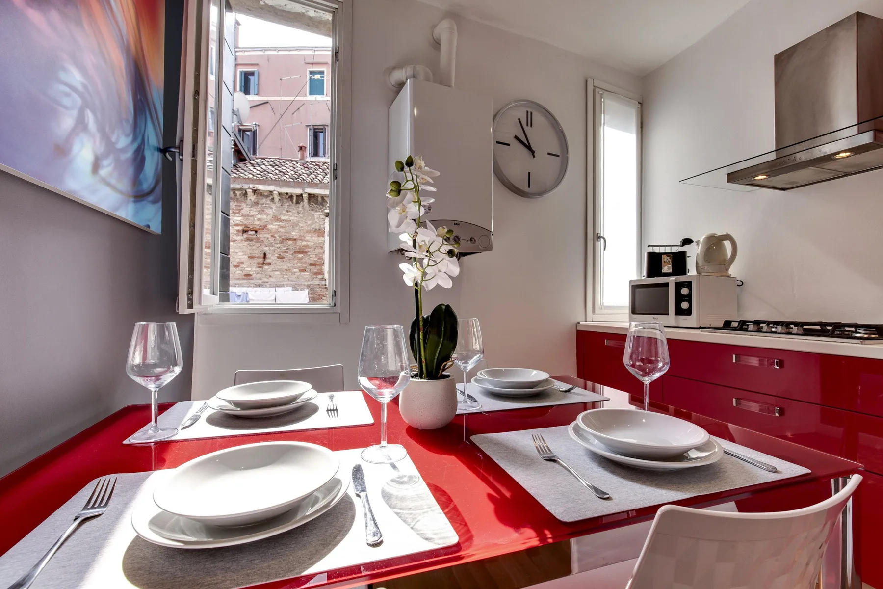 A bright dining area with a red table set for a meal beside two windows.