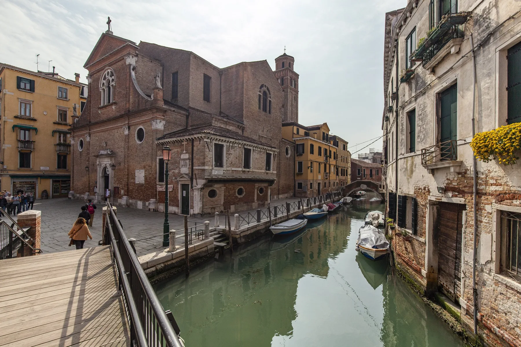 A canal runs between historic buildings, with a pedestrian walkway and small boats along the water.