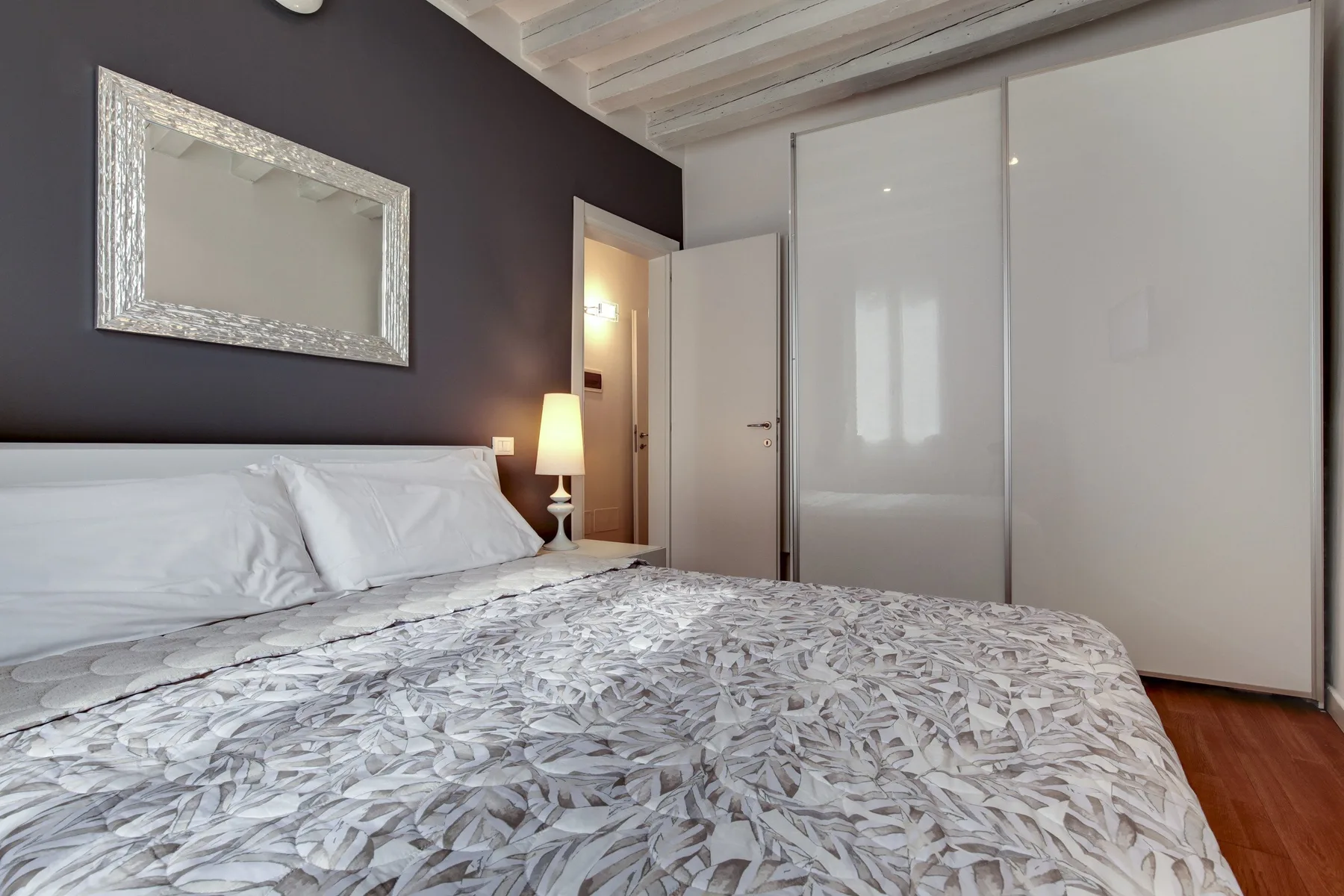 A bedroom with a bed beneath a dark wall and a framed mirror.