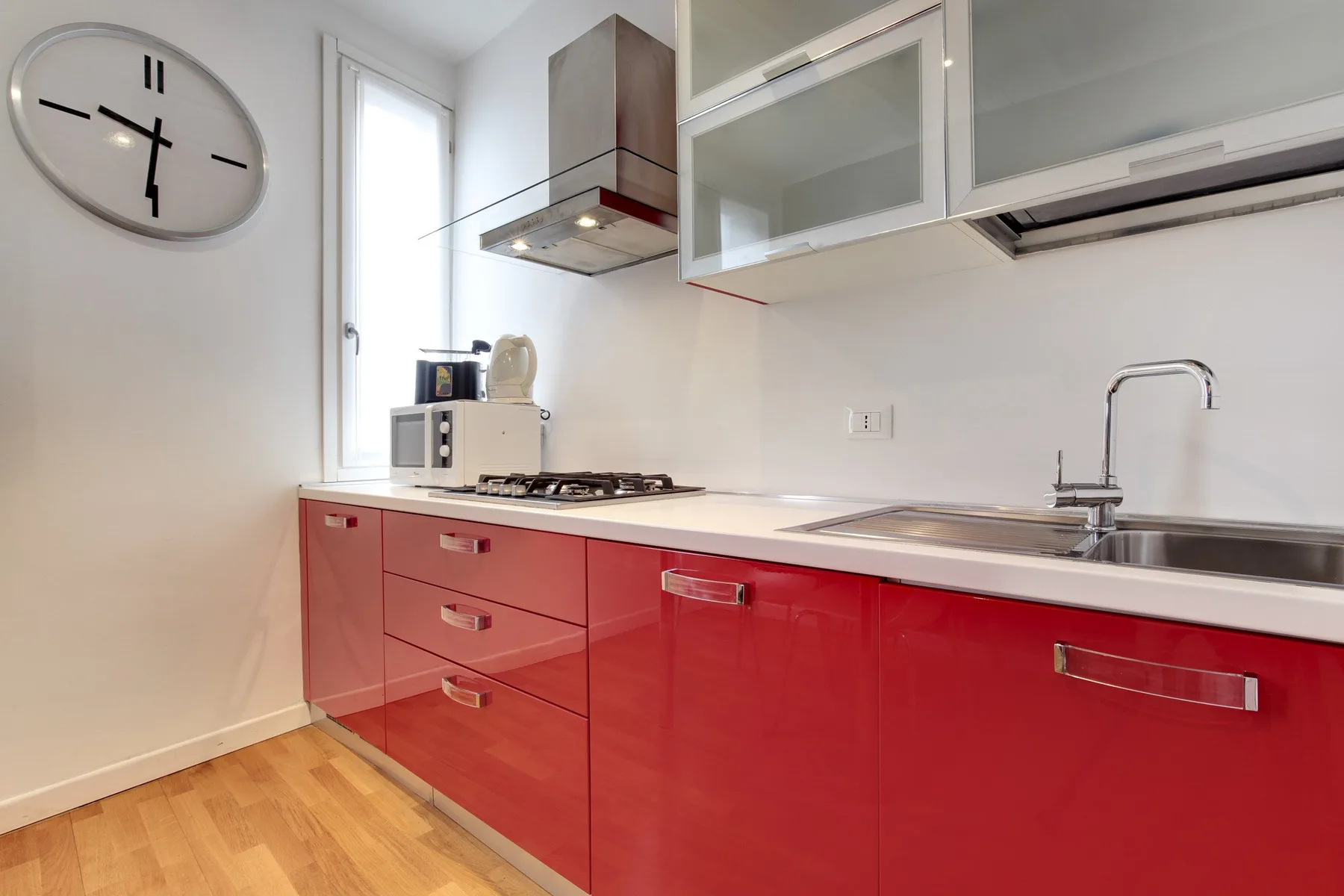 A bright modern kitchen with red cabinets and a stainless-steel sink.