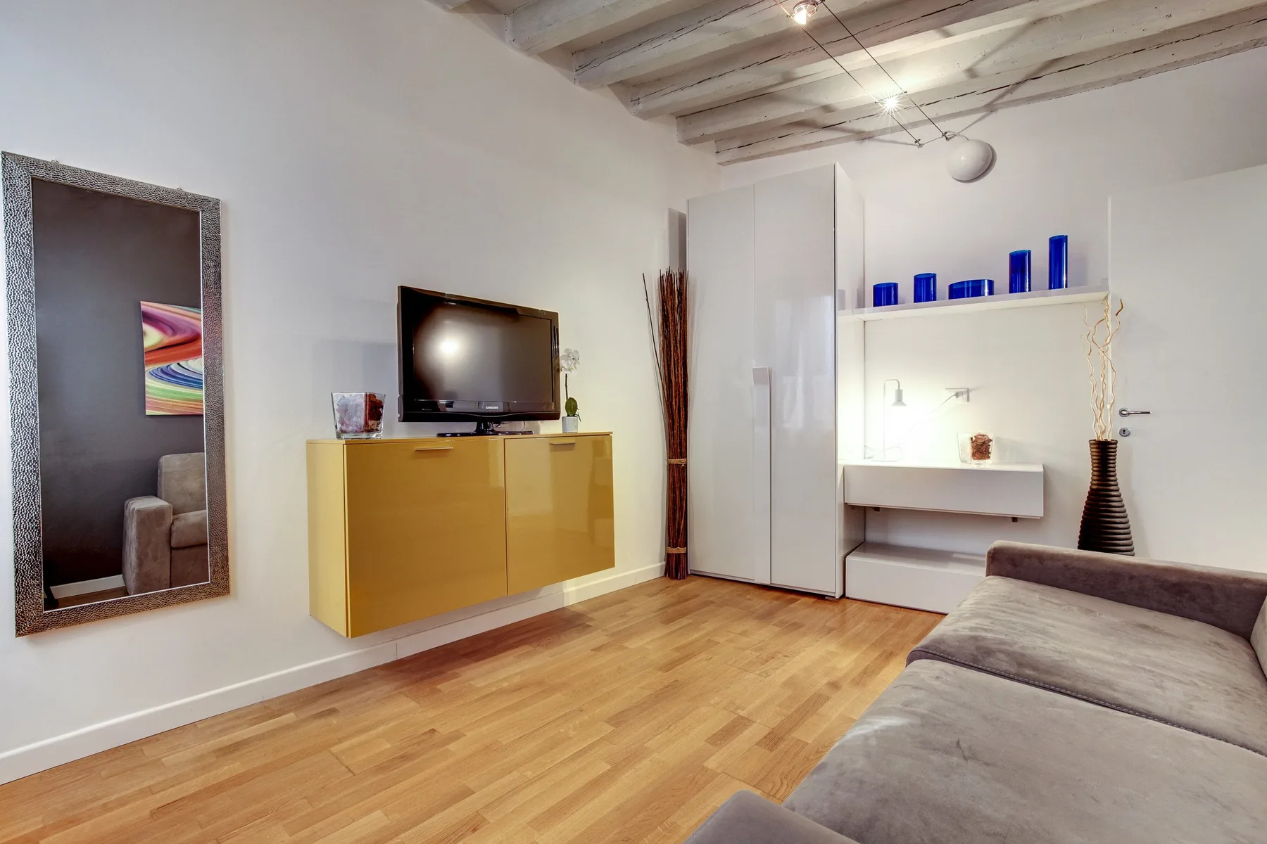 A bedroom with a bed, wall-mounted television, and light wood flooring.
